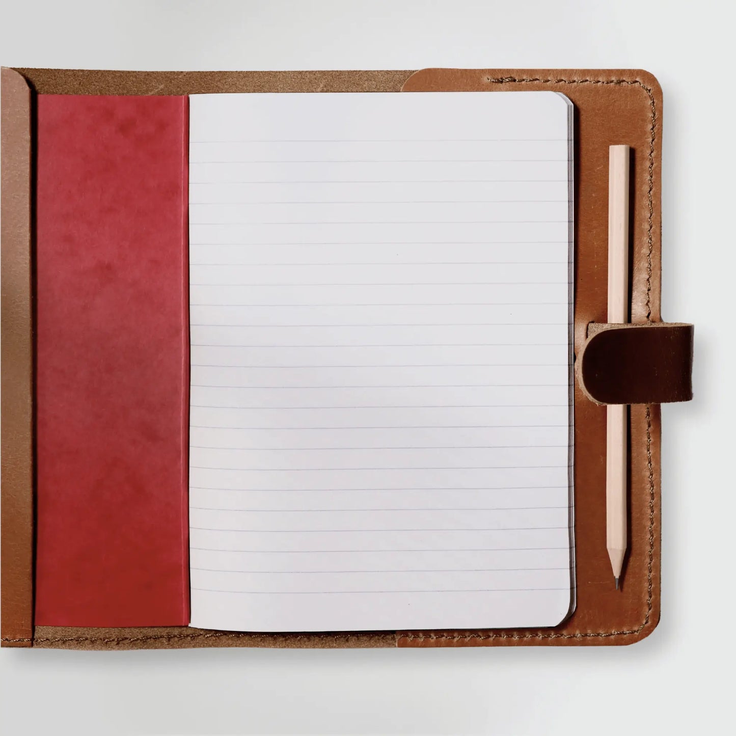 Inside of genuine leather notebook showcasing quality craftsmanship with lined paper, pencil holder, and red interior cover. New Zealand-made in timeless tan leather.