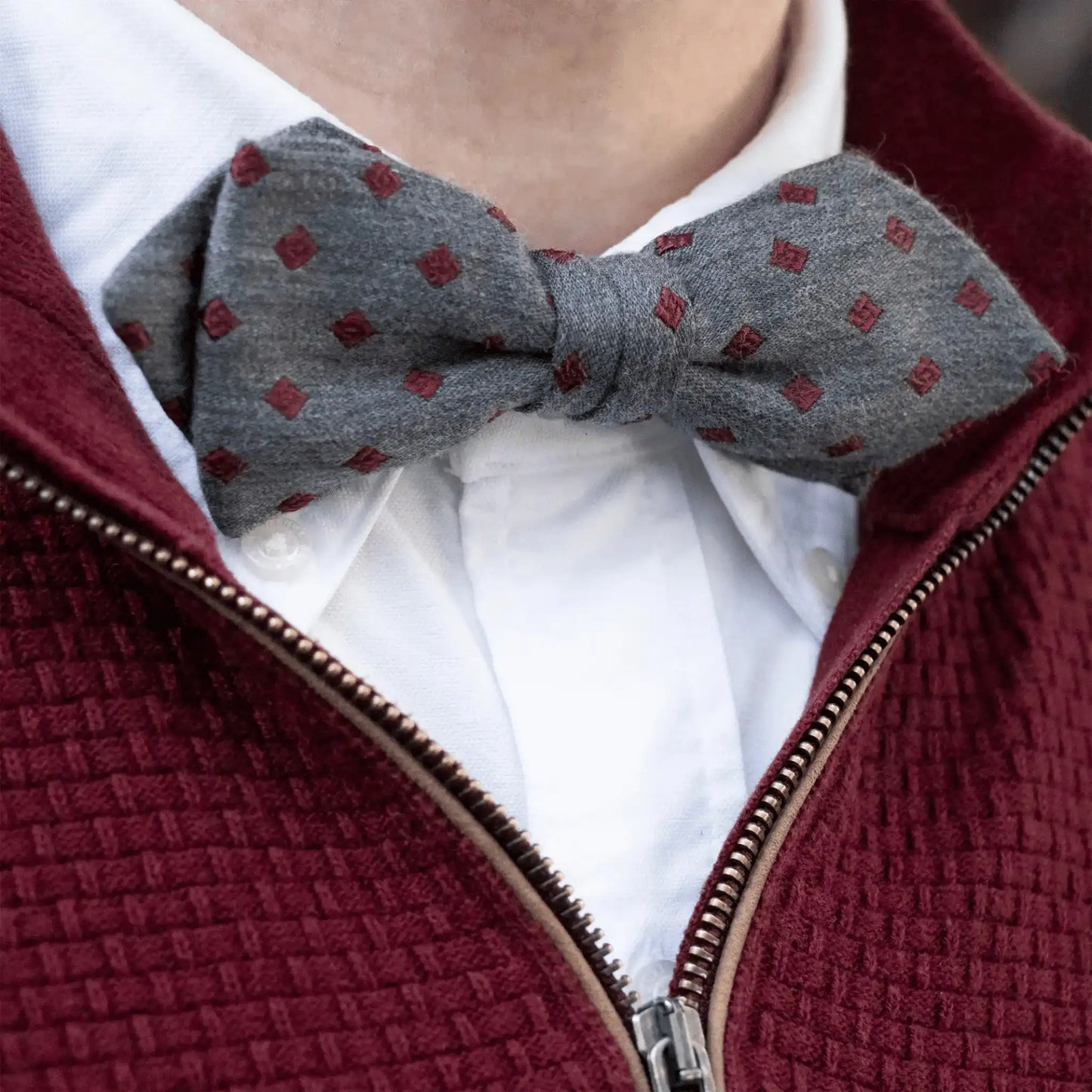 Grey marle bow tie with burgundy diamond pattern, styled with a white button-down shirt and burgundy woven zip-up jumper—New Zealand men's accessory.