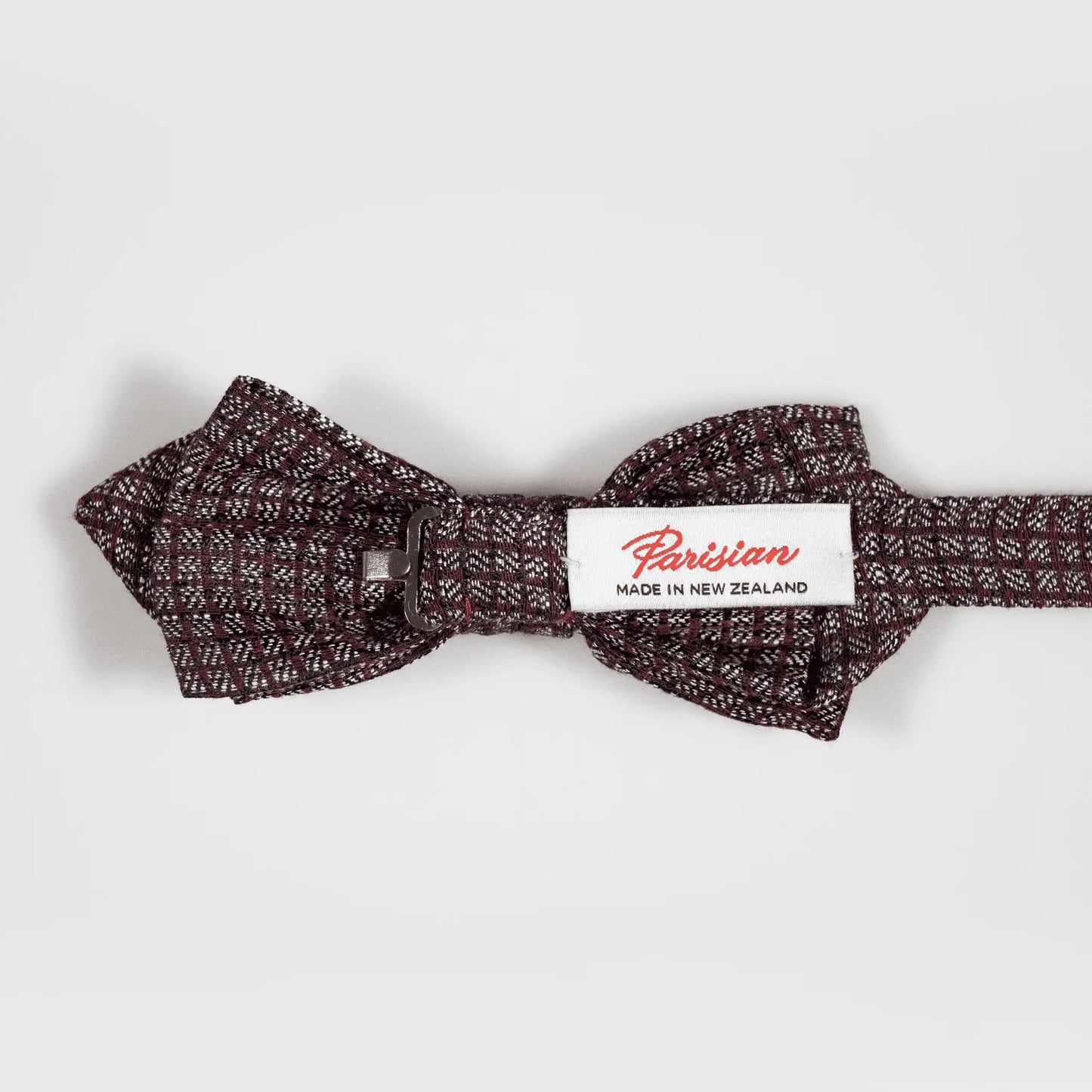 View of the back of the burgundy and grey micro squares bow tie showing the "Parisian Made in New Zealand" woven label, highlighting superior quality.