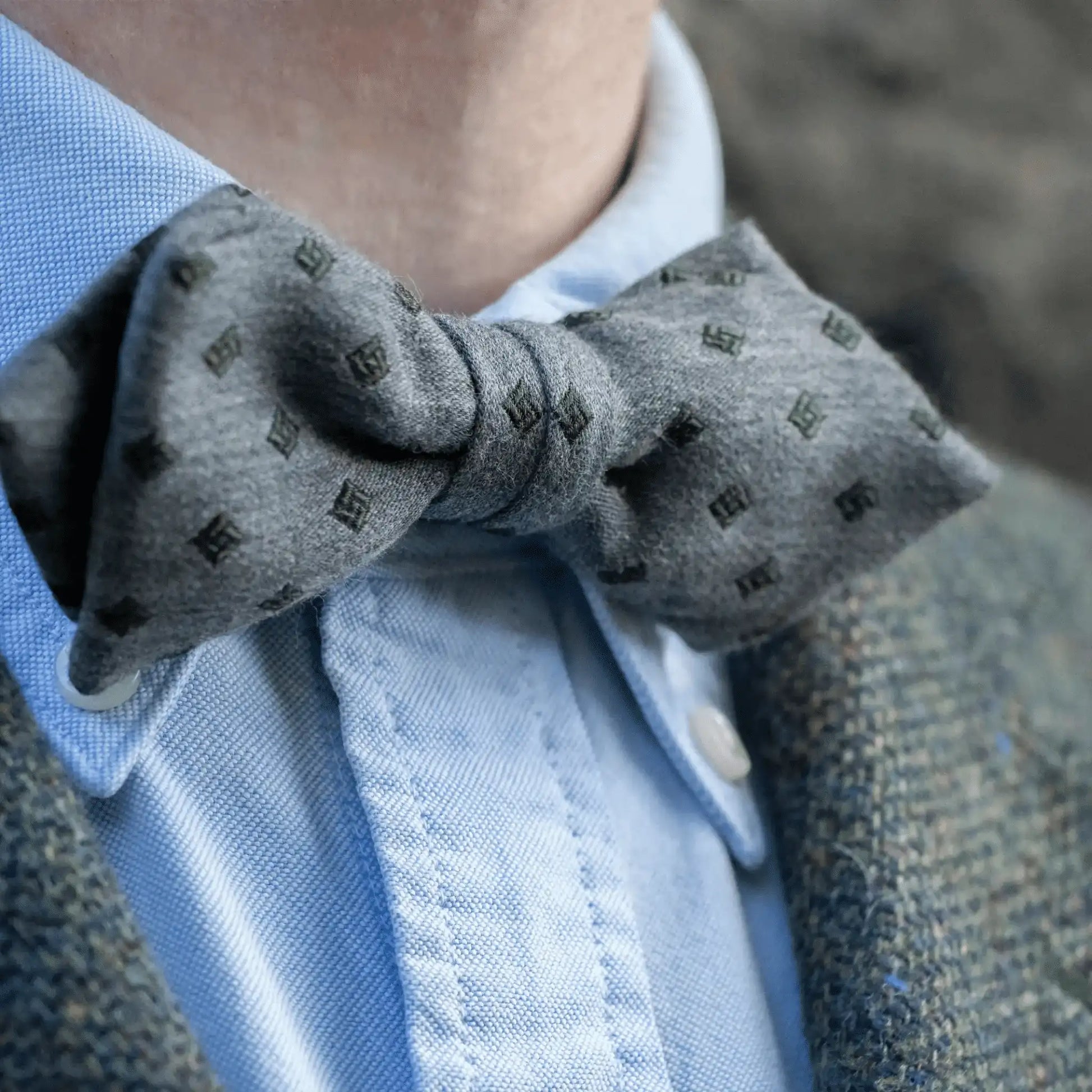 Elegant grey marle bow tie with olive diamond pattern on model, paired with tailored blue button-down shirt and textured grey woven blazer—New Zealand men's accessory.