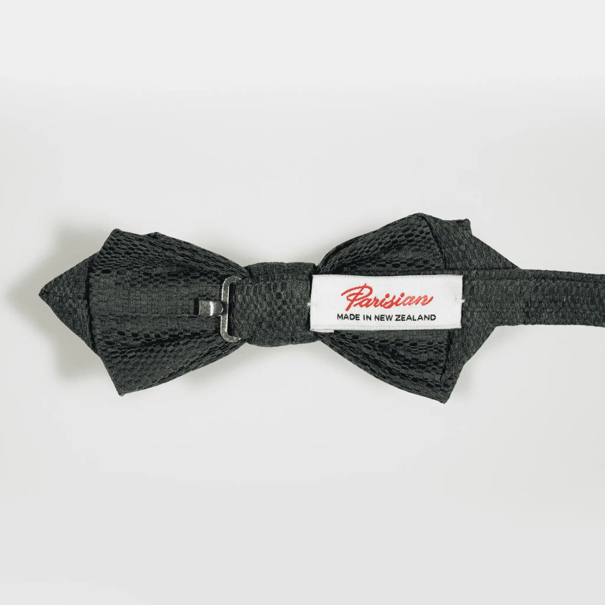 'Parisian Made in New Zealand' woven label shown on the back of an olive green and navy blue Jacquard pattern bow tie.
