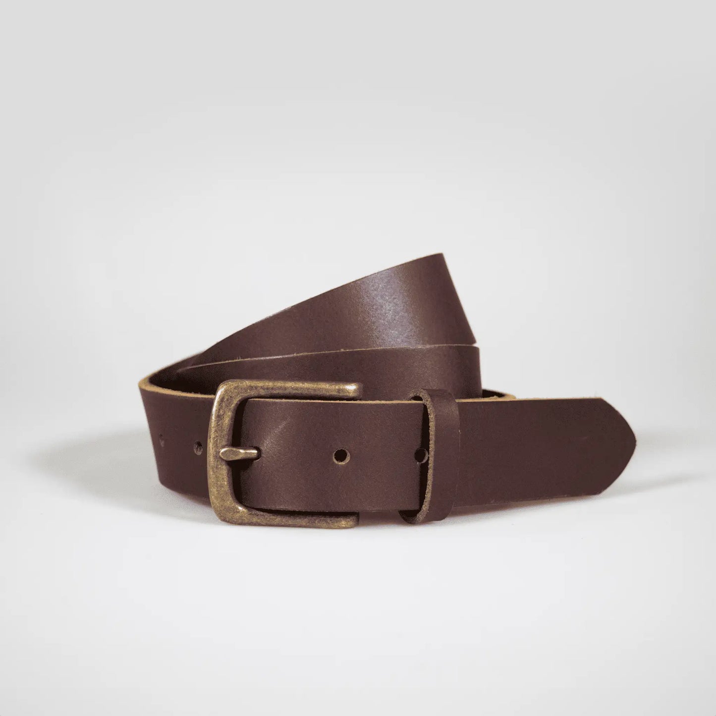 Brown classic leather belt, rolled up on white surface—expertly designed and made in New Zealand, blending functional elegance with rich leather texture.