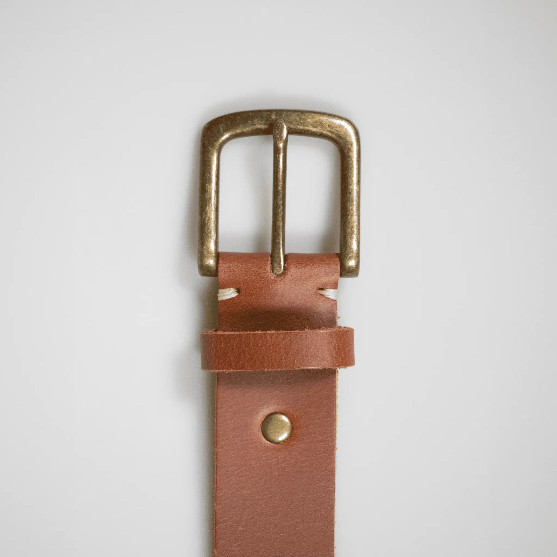 Close-up of simple brass buckle on a tan brown men's belt—made in New Zealand with genuine leather for a long lasting, timeless accessory.
