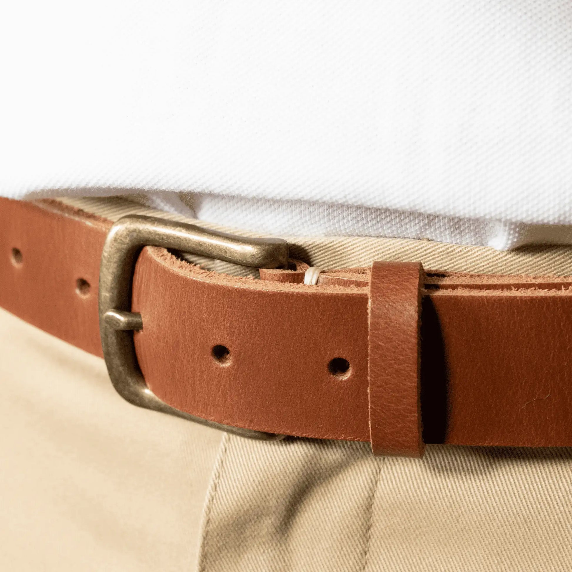 Close-up of men's classic tan leather everyday belt with simple brass buckle, paired with tan chinos and a white t-shirt.