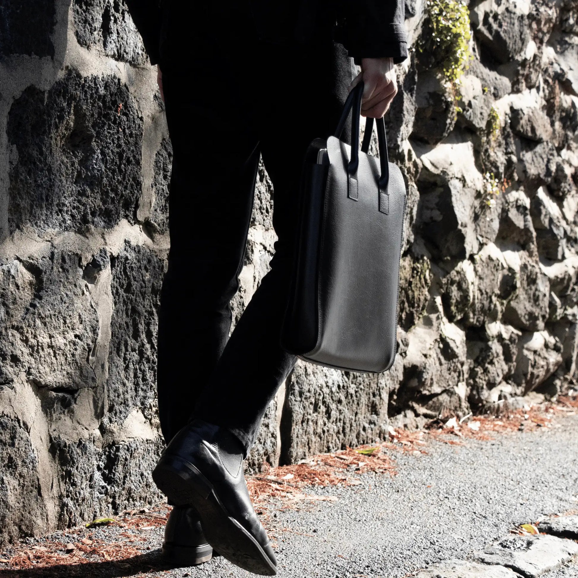 Man walking in sunlight with Black Leather Business Tote—expertly crafted in New Zealand, blending function with fine leather elegance.