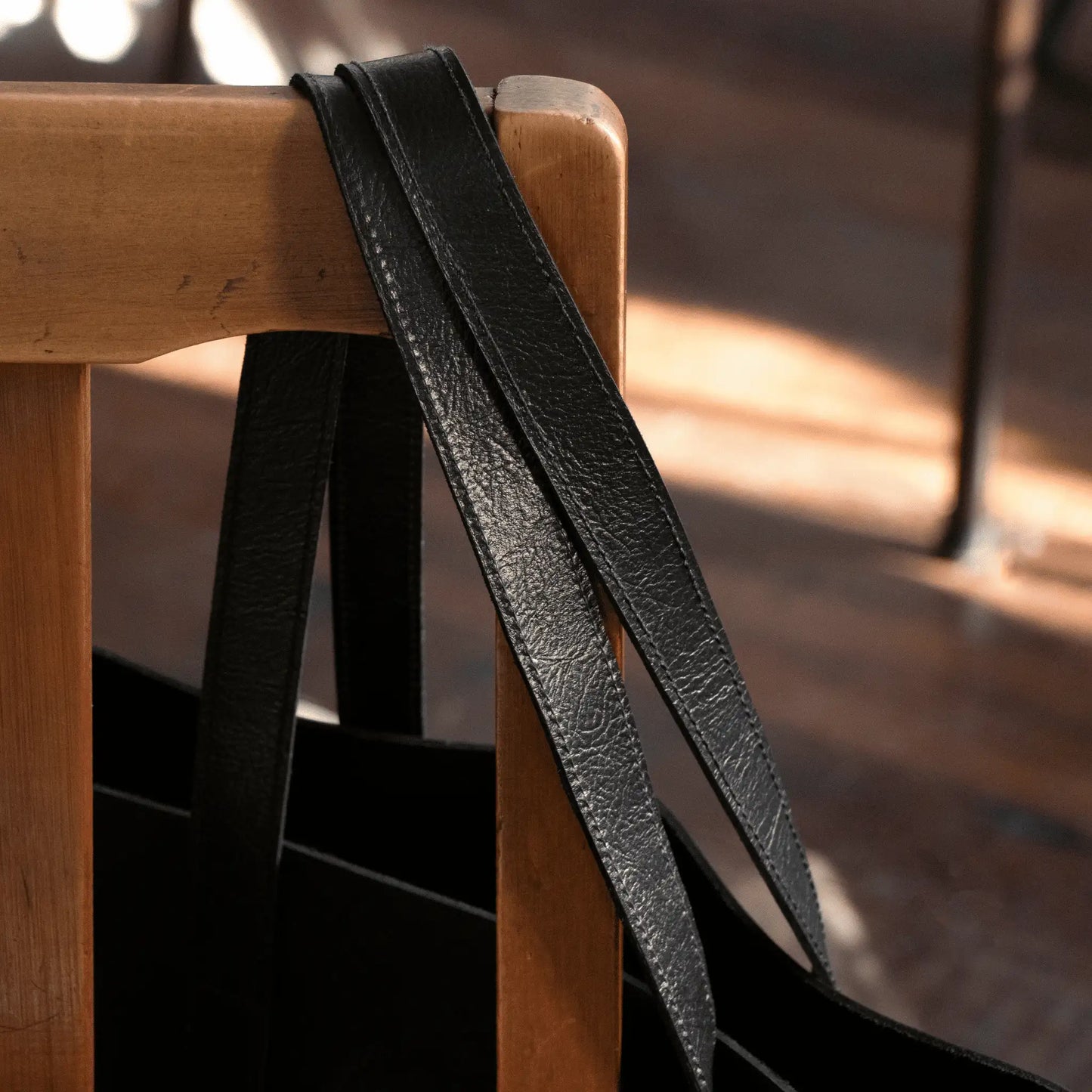 Close-up of Black Leather Everyday Tote hanging from wooden chair, crafted locally in New Zealand from genuine leather for a timeless accessory.