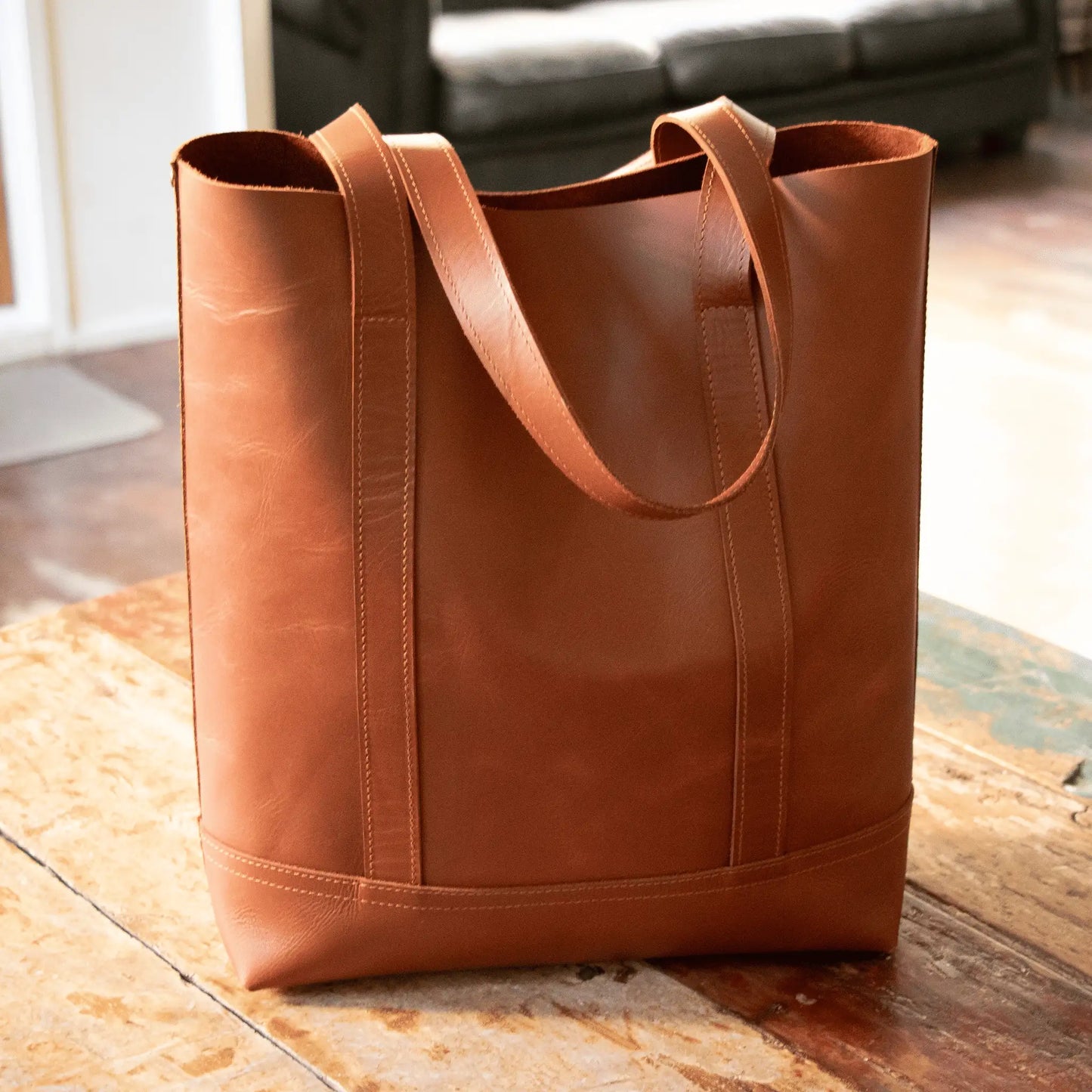 NZ-made tan leather tote on rustic wooden table in sunlight, showcasing expert craftsmanship and timeless, simple design.