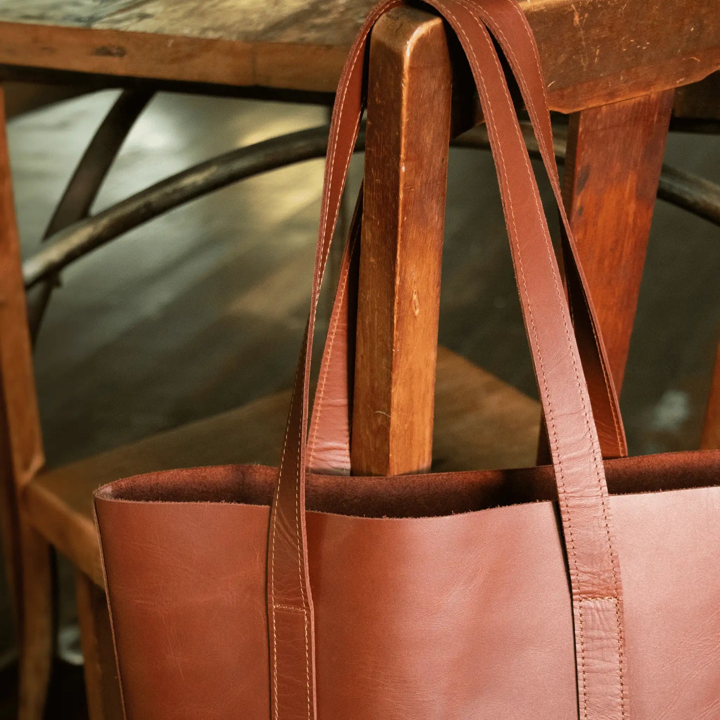 Tan Leather Everyday Tote hanging on wooden chair, highlighting refined stitching and quality leather—small batch, made to last.