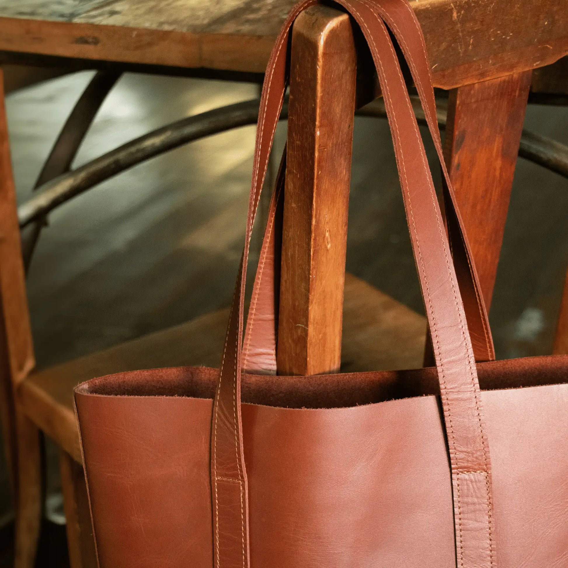 Tan Leather Everyday Tote hanging on wooden chair, highlighting refined stitching and quality leather—small batch, made to last.