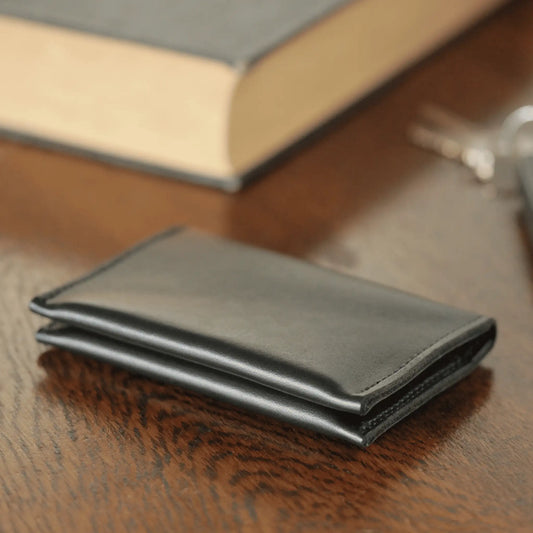Black leather folded card wallet sitting on a wooden table, showcasing its sleek design and quality craftsmanship.