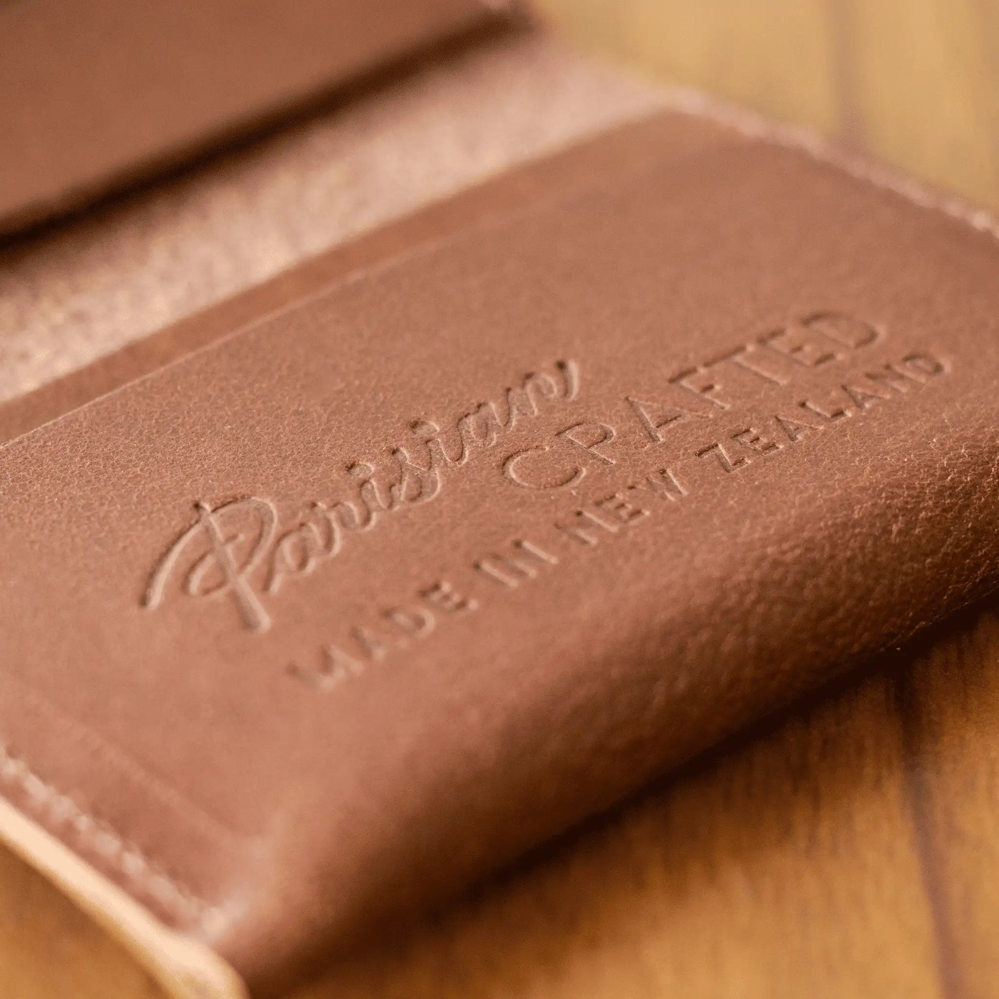 Close-up of the embossed "Parisian Crafted Made in New Zealand" text inside a tan leather folded card wallet, highlighting premium craftsmanship.