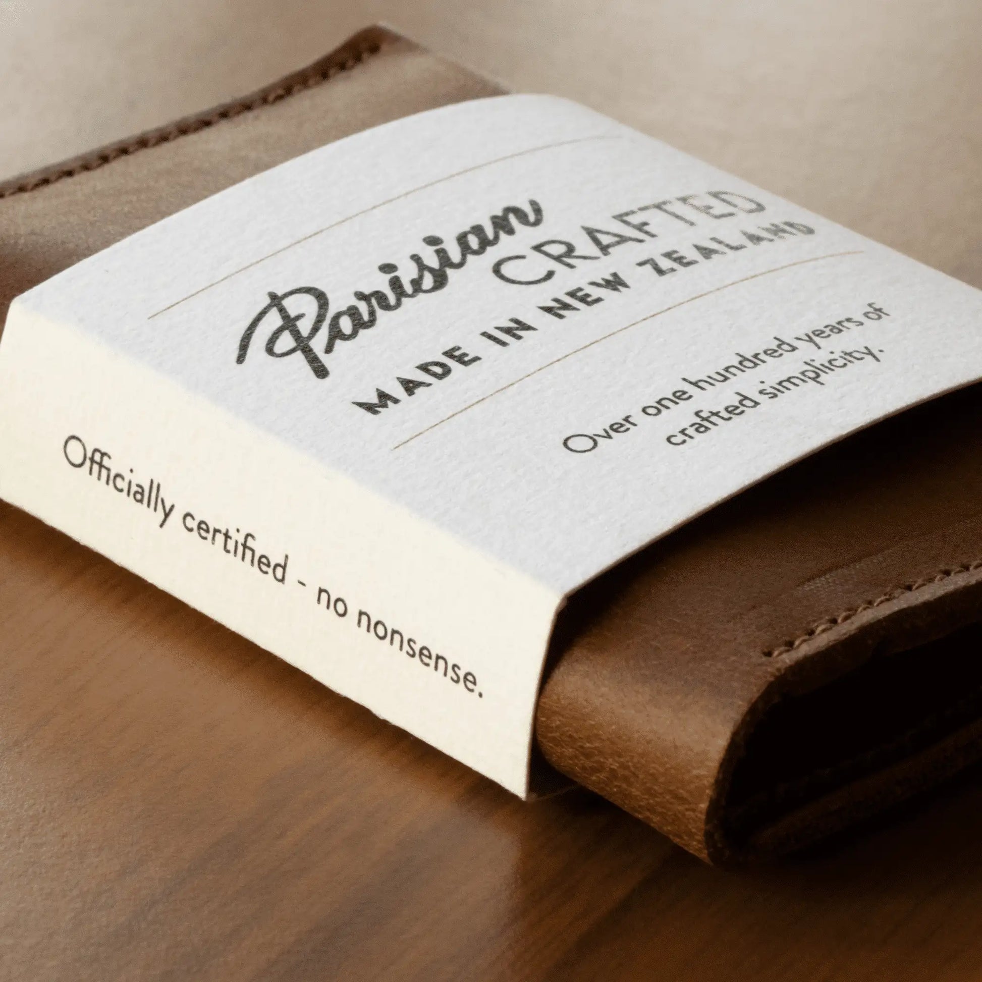 Close-up of a tan leather folded card wallet wrapped in white card packaging, showcasing sleek design and quality craftsmanship.
