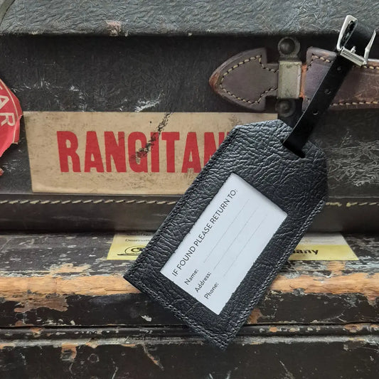 Black leather luggage tag on a vintage suitcase with 'Rangitani' branding.