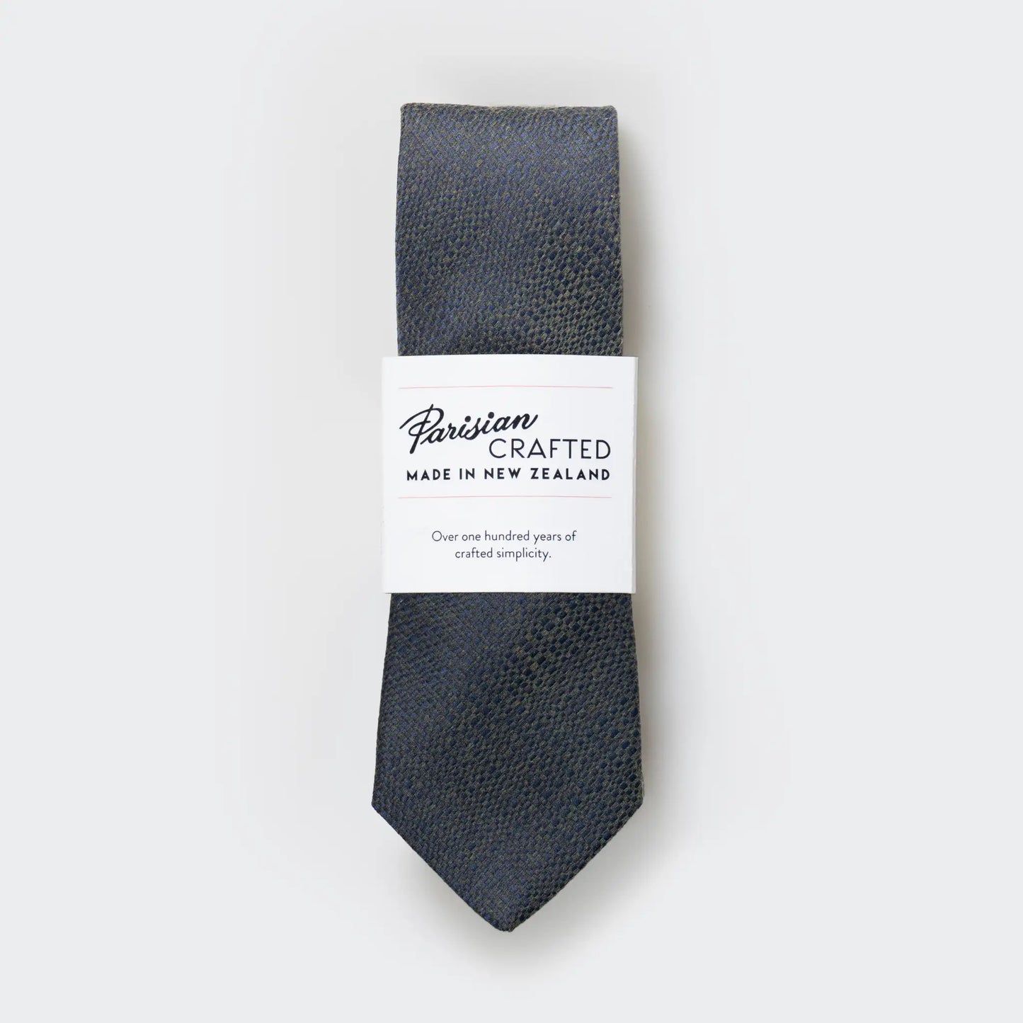 Olive green and navy blue tie in a textured cotton-blend, folded into a sleek white packaging sleeve with bold Parisian Crafted logo.
