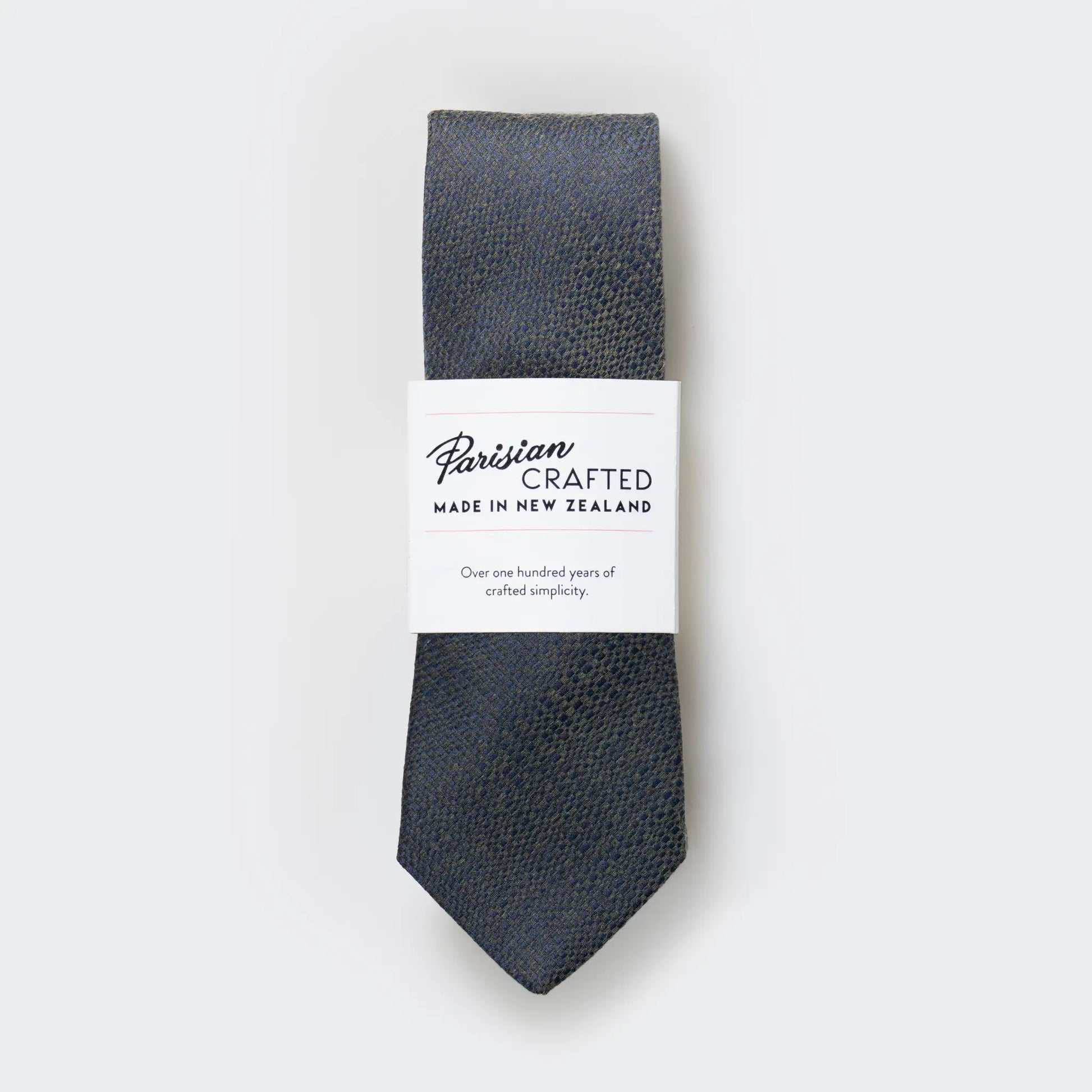 Olive green and navy blue tie in a textured cotton-blend, folded into a sleek white packaging sleeve with bold Parisian Crafted logo.