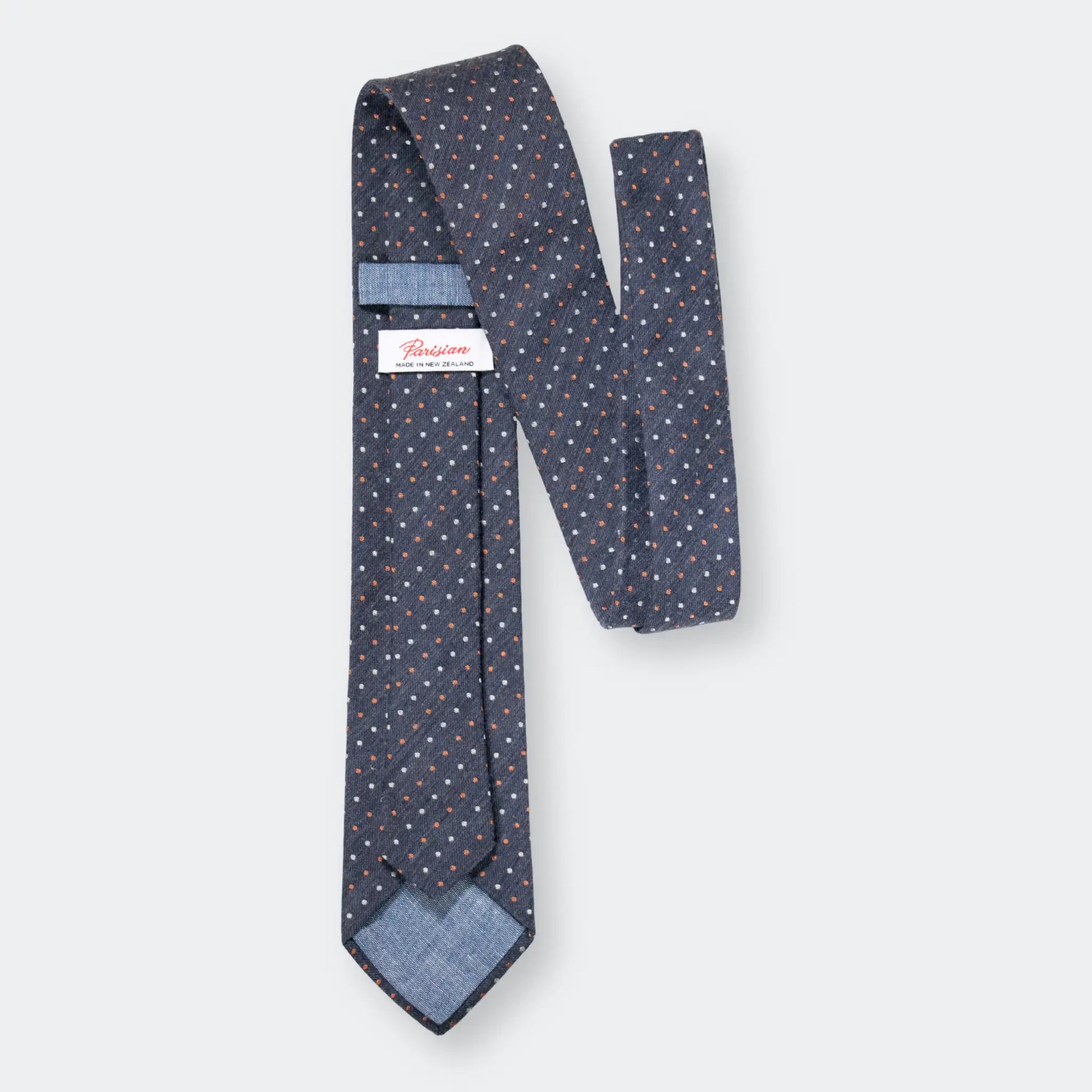 Back of a denim blue necktie with white and rust coloured pin-dot pattern, with 'Parisian Made in New Zealand' woven label on show.