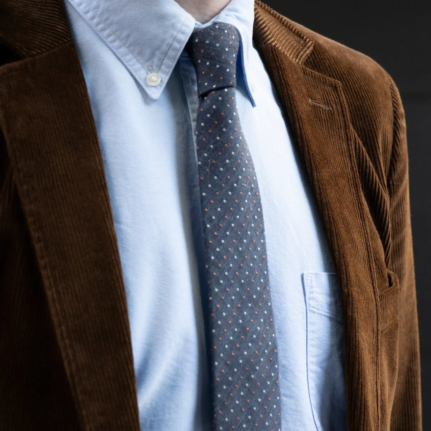 Close-up of the Denim White Rust Pin Dot Tie worn with a blue button-down shirt and brown corduroy jacket, highlighting its rugged texture and thoughtful detailing.