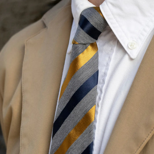 Close-up of the grey tie with gold and navy satin stripes, paired with a white-shirt and tan blazer - stylish simplicity for men.
