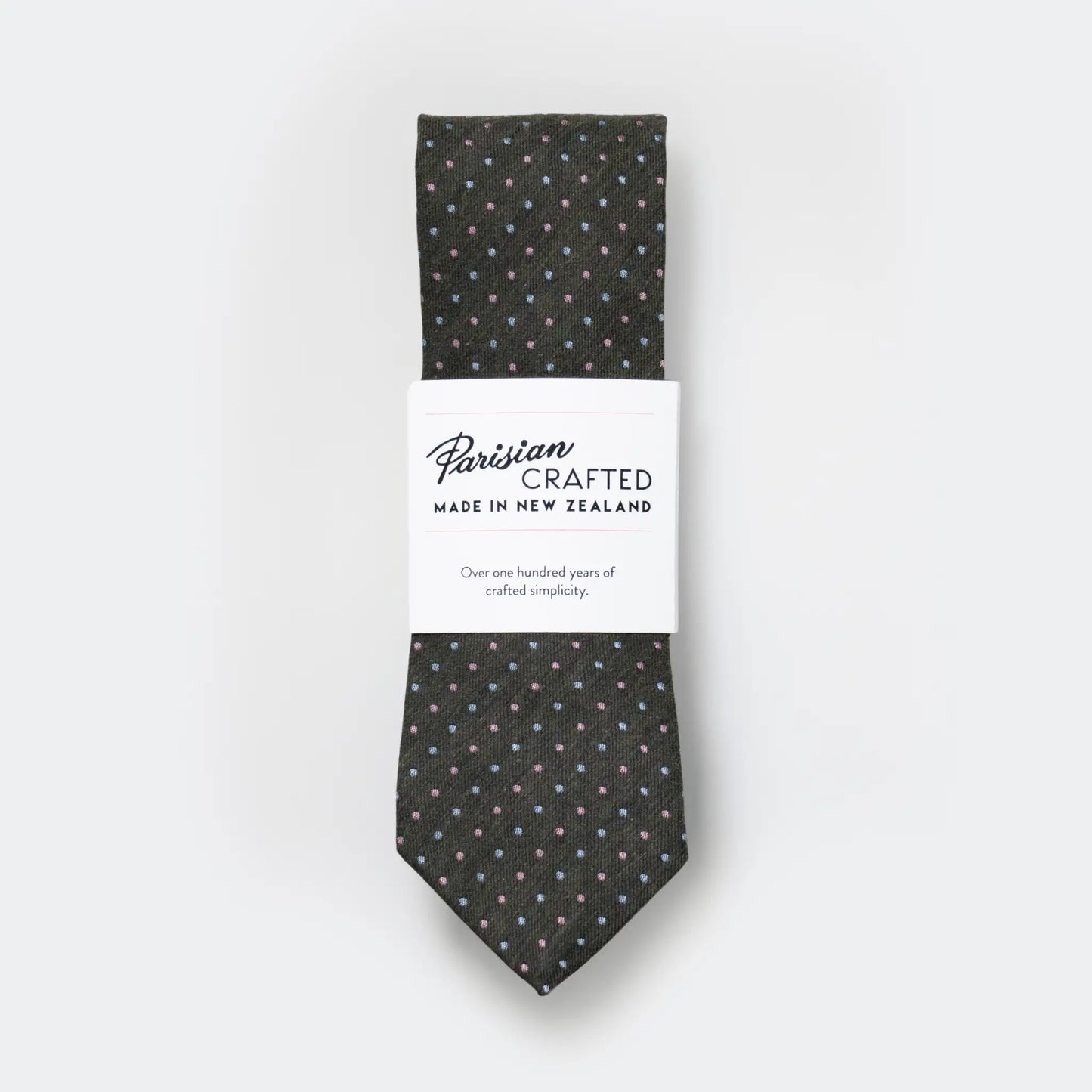Olive green tie with sky and pink pin-dot design, folded into Parisian Crafted's white packaging sleeve with bold logo - crafted locally in Auckland.