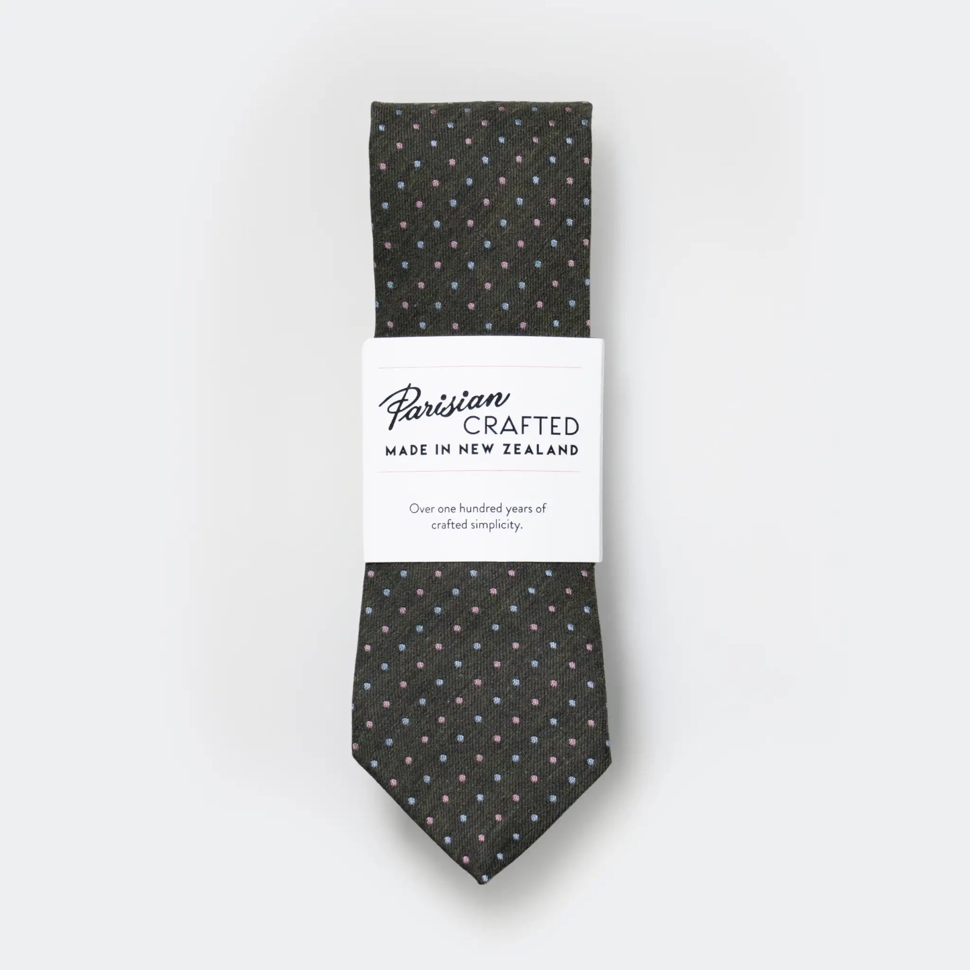 Olive green tie with sky and pink pin-dot design, folded into Parisian Crafted's white packaging sleeve with bold logo - crafted locally in Auckland.