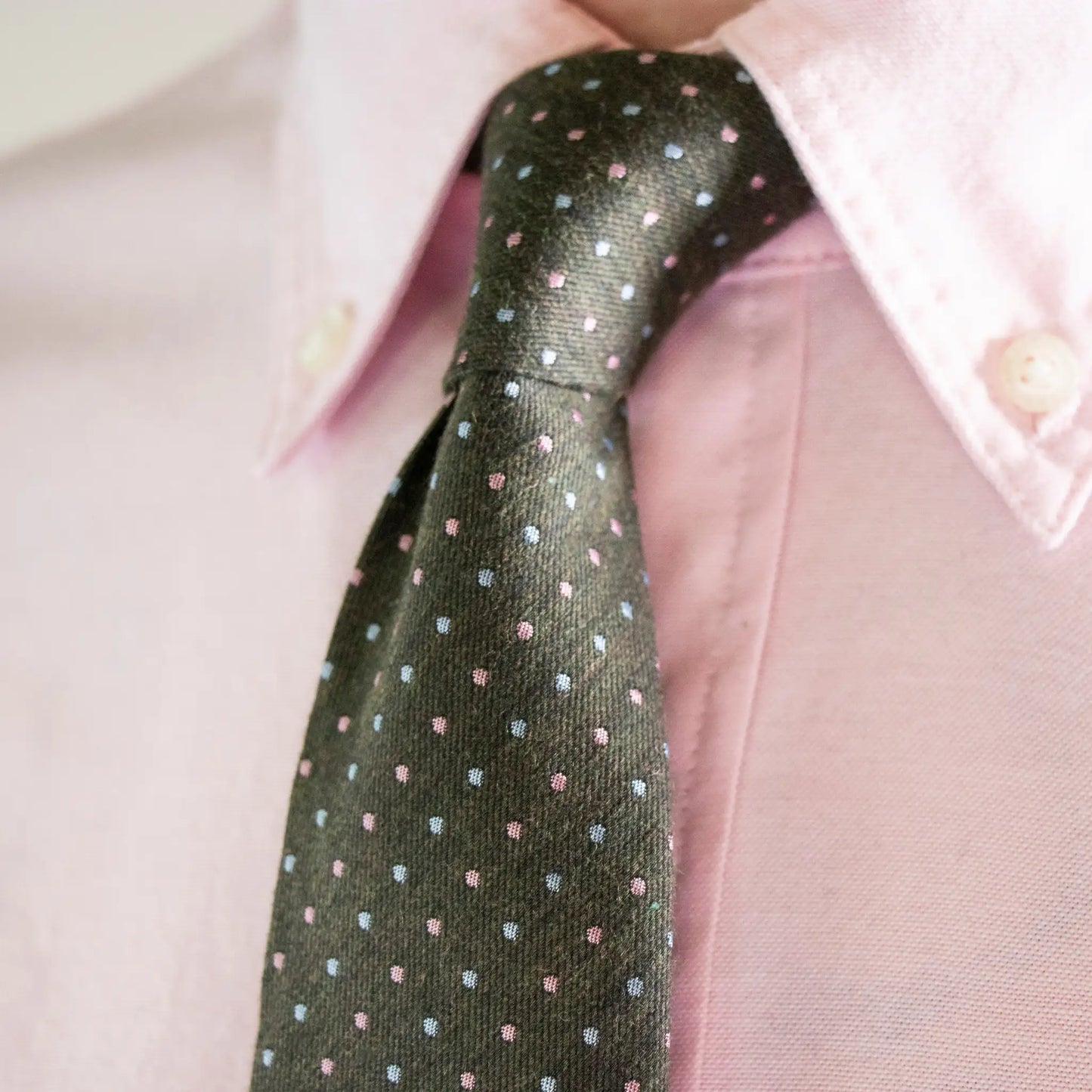 Close-up of olive green sky and pink pin-dot tie, showcasing it's simple design and everyday work-wear style.