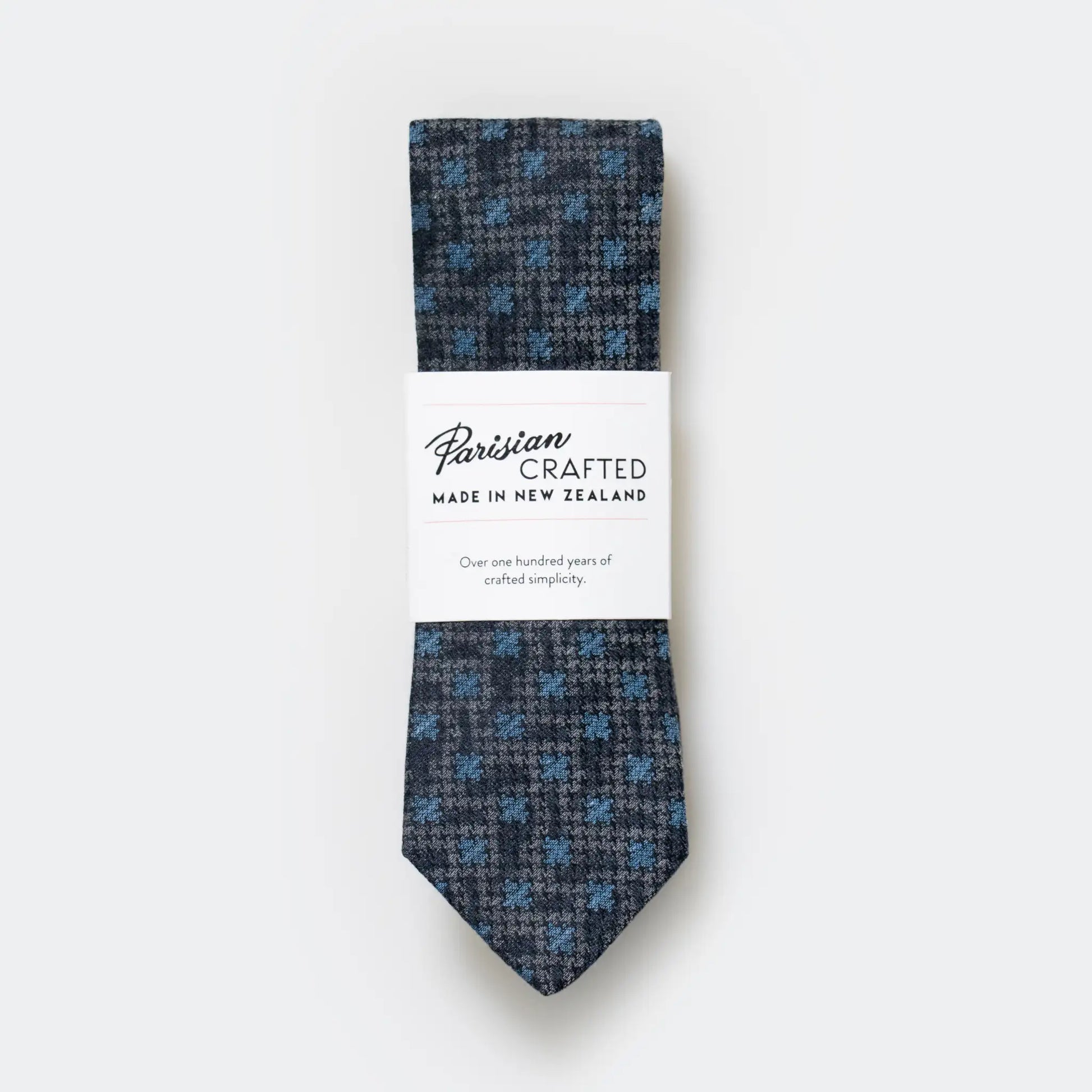 Slate blue abstract houndstooth designed tie folded into Parisian Crafted's simple packaging sleeve with bold logo.