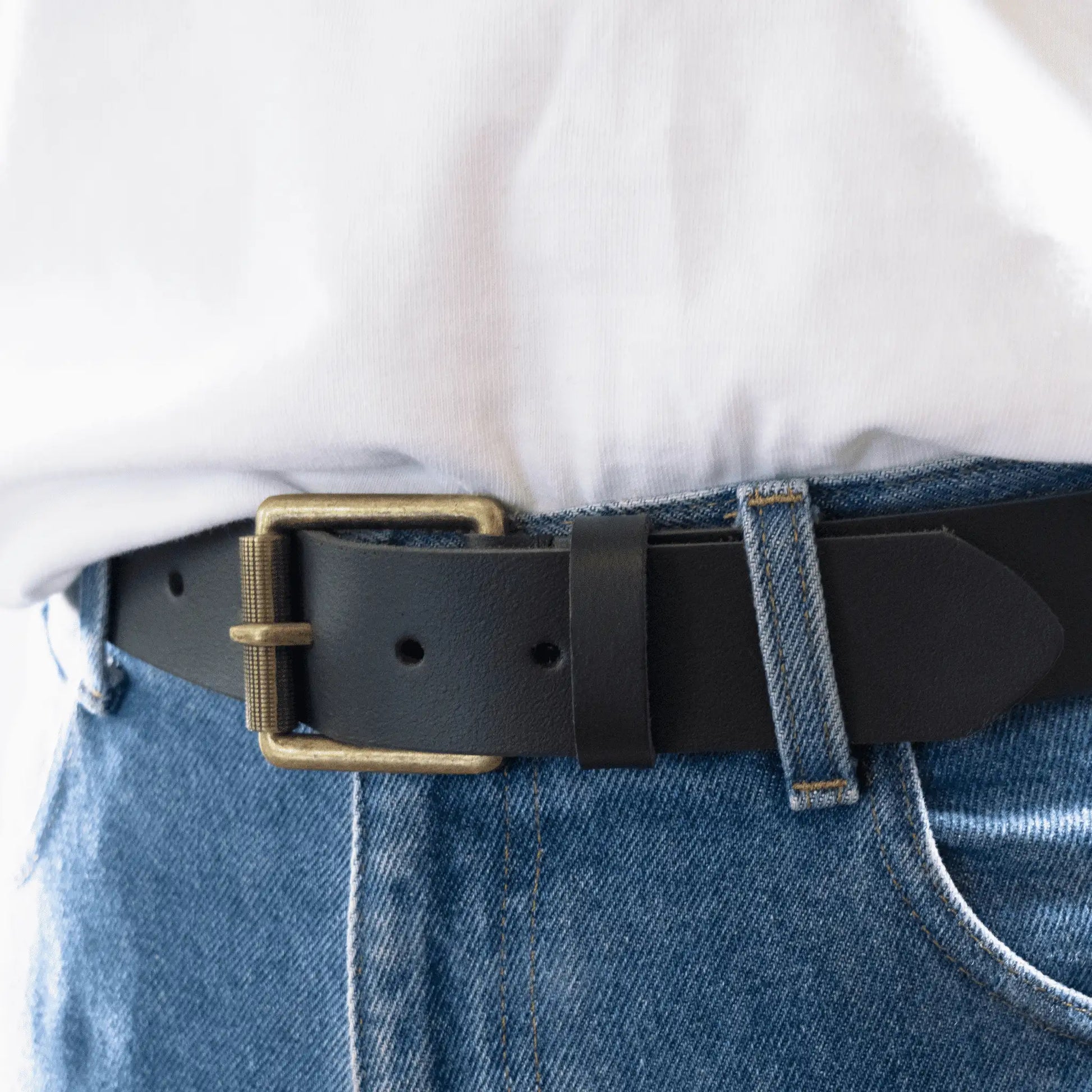 Close-up of men's black leather belt styled simply with jeans and white t-shirt - showcasing a brass buckle and crafted leather.
