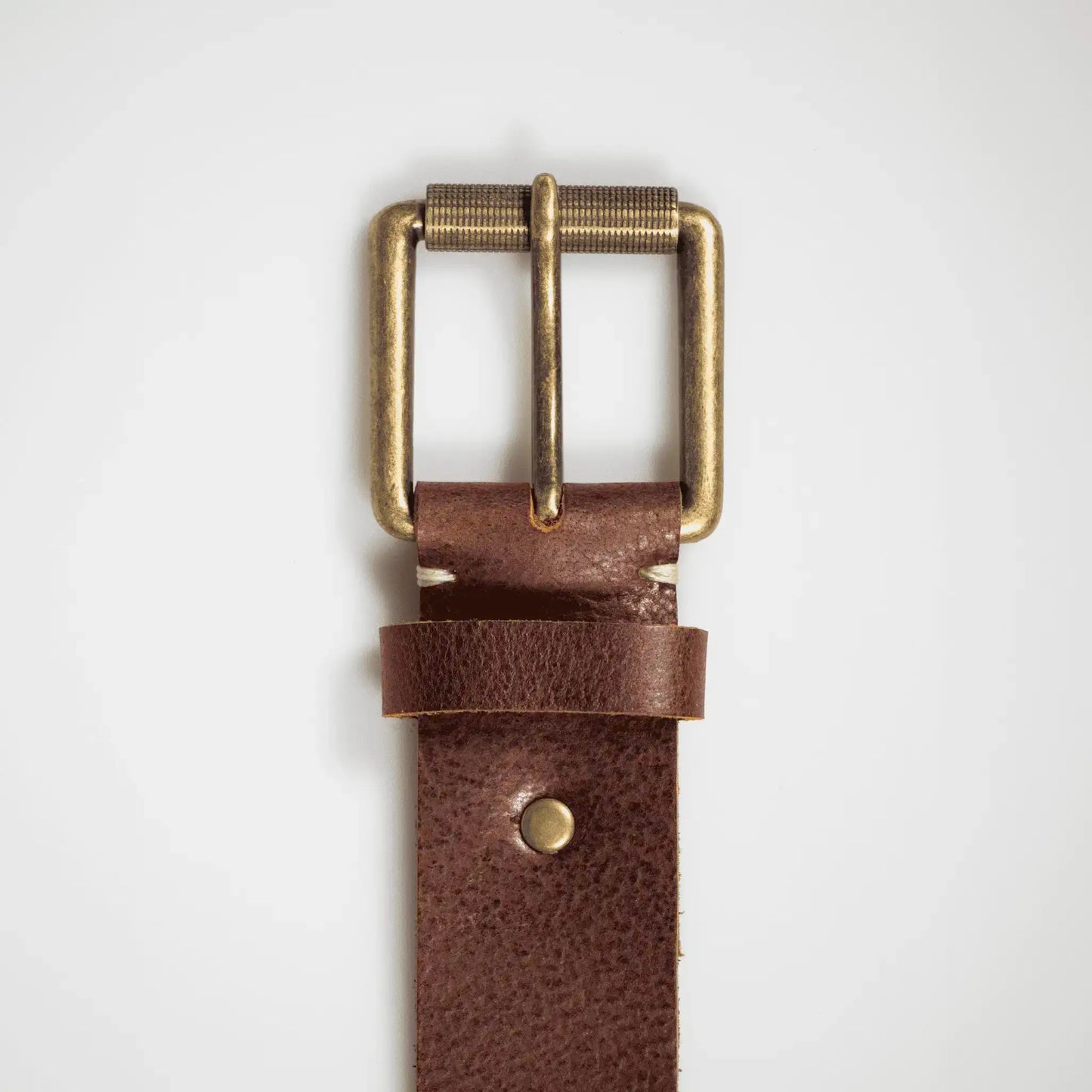Close-up of brass hardware on mocha-brown leather belt, highlighting refined stitching and quality leather.