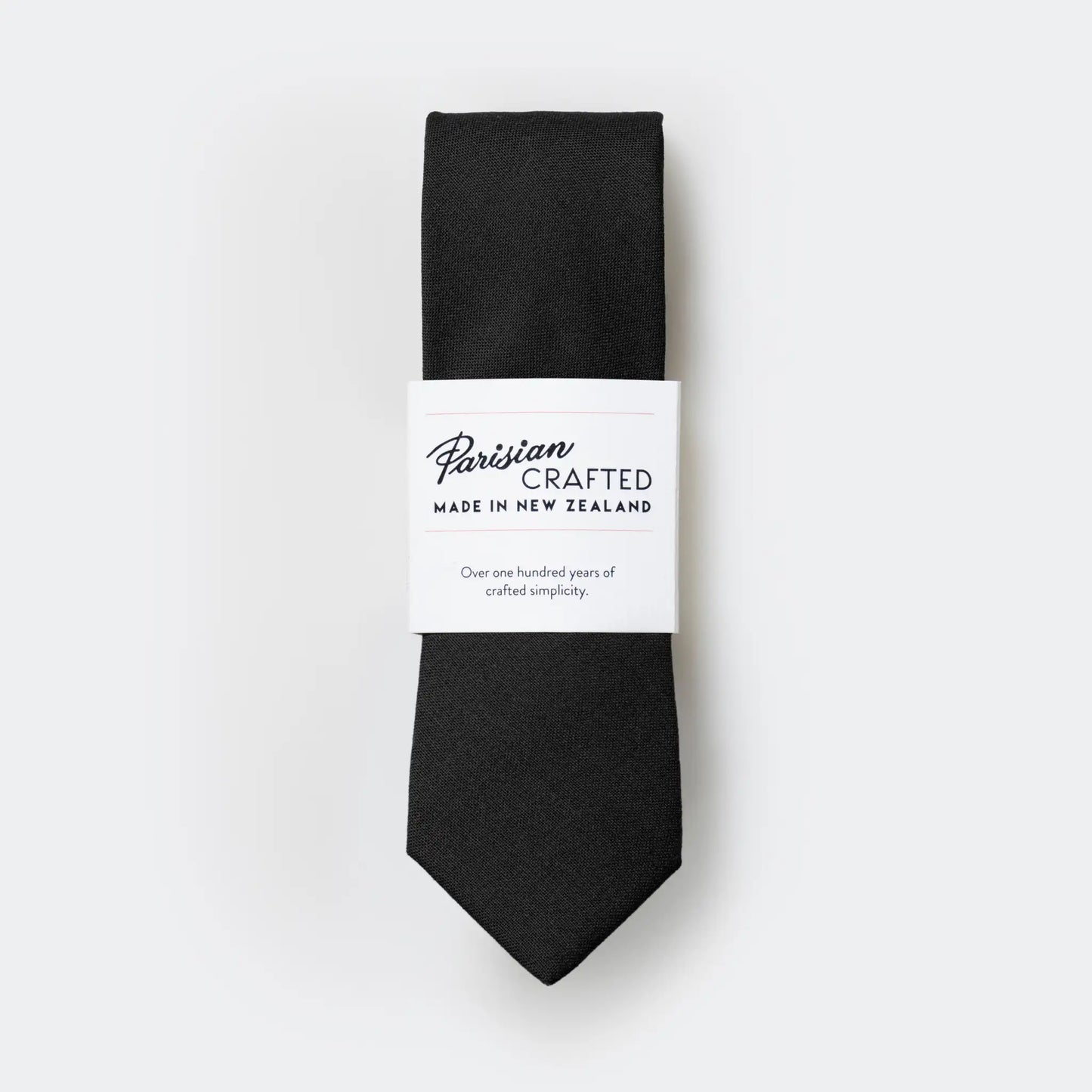 The pure black worsted wool tie folded and packaged in Parisian Crafted's simple white sleeve with bold logo.