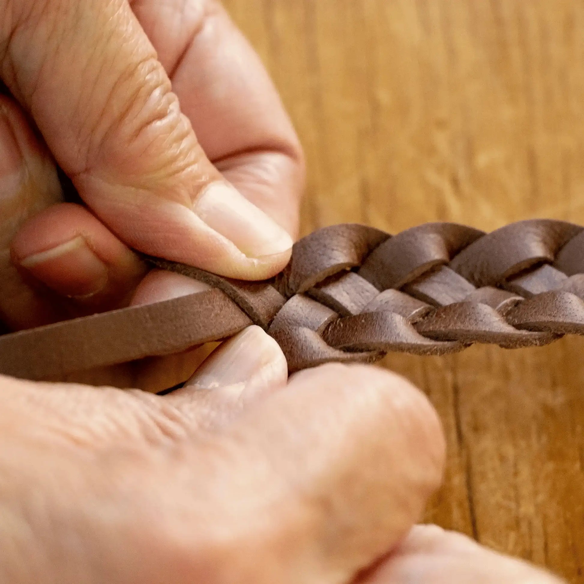 Close-up of hands weaving a Parisian Crafted tan leather belt, highlighting the quality and detailed hand-weaving process.