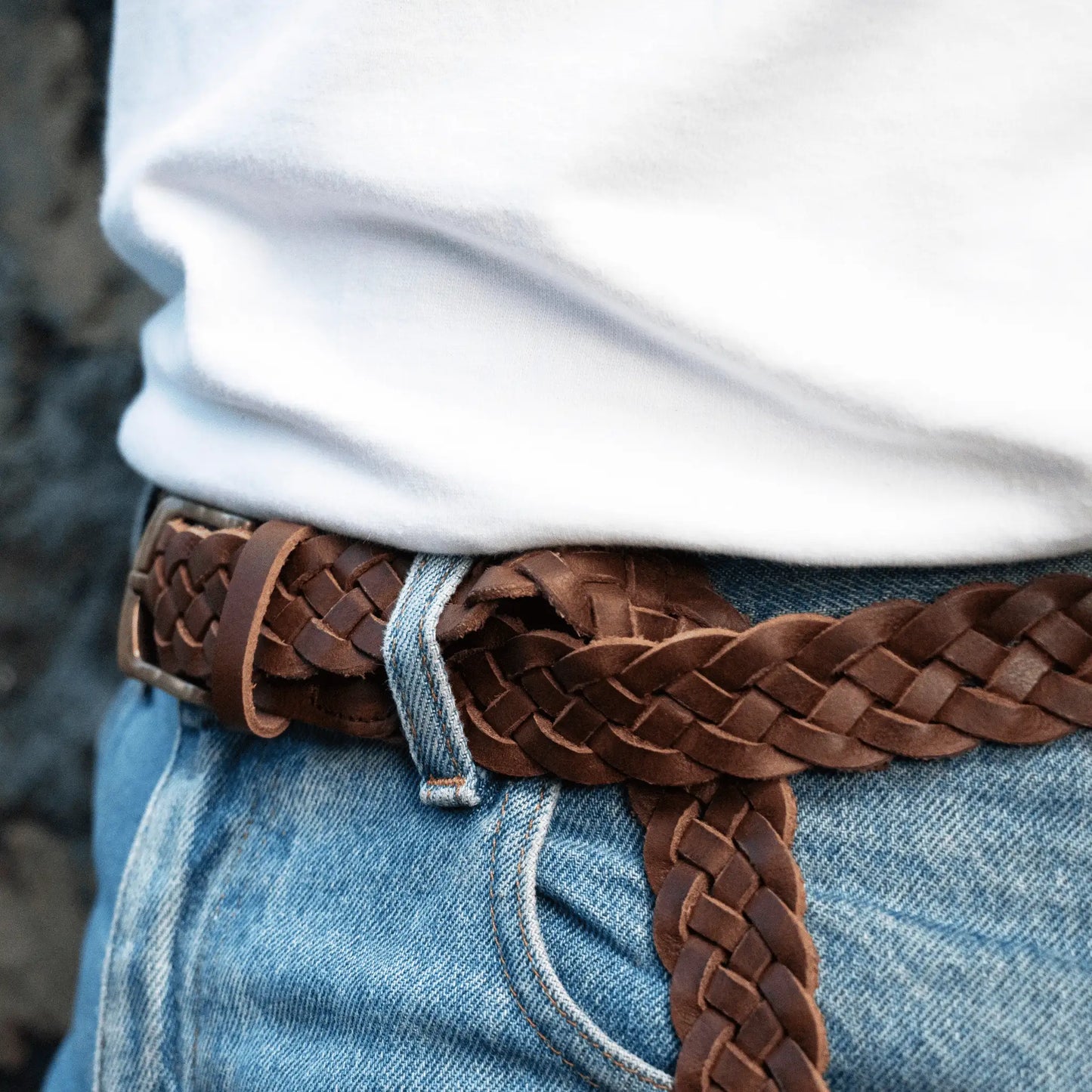 Close-up of hand-woven brown leather men's belt, showing the intricate plaited design and brass buckle.