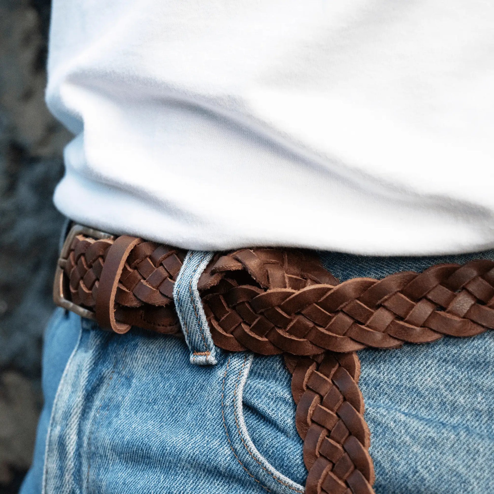 Close-up of hand-woven brown leather men's belt, showing the intricate plaited design and brass buckle.