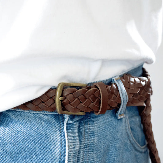 Close-up showing brass buckle and intricate detail of a hand-woven leather belt in brown. Paired with jeans and a white tee for a stylish smart-casual men's look.