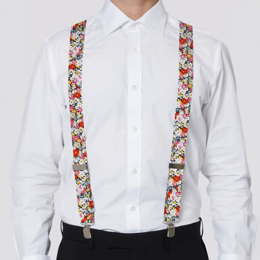 Person wearing a white shirt with colorful Liberty floral suspenders on a plain background