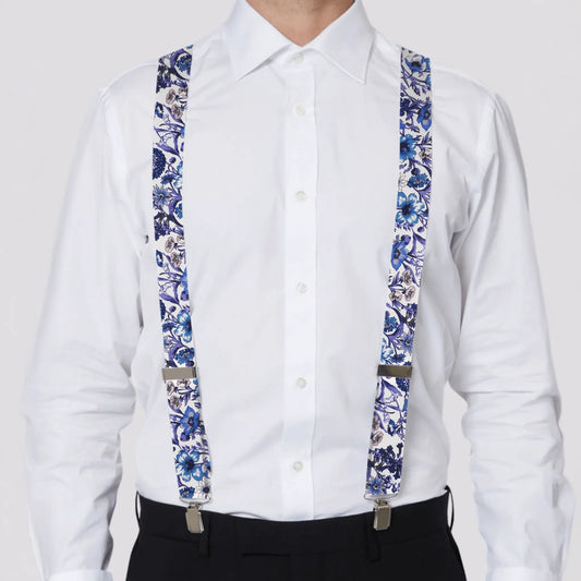 Person wearing a white shirt with blue and purple floral suspenders on a plain background