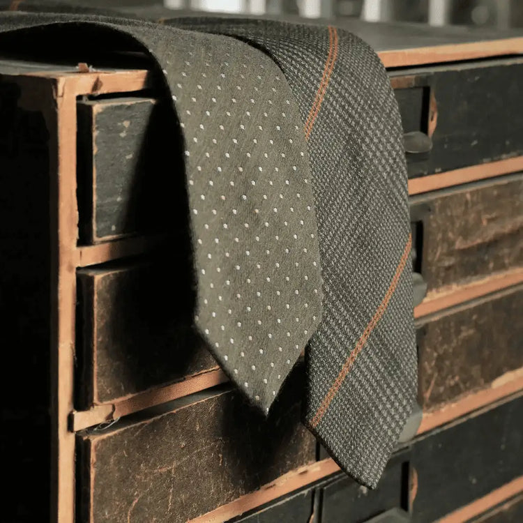 Two woven ties with different patters draped over the edge of a wooden unit with drawers
