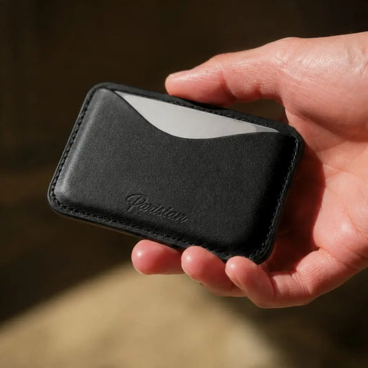A close-up of a hand holding a slim black leather card holder wallet with a white card partially inserted. The brand name 'Parisan' is embossed on the front.