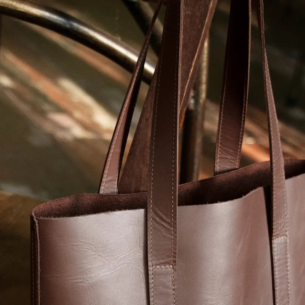 Chestnut brown leather tote bag with handles against a blurred background