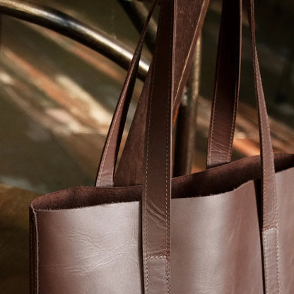 Chestnut brown leather tote bag with handles against a blurred background