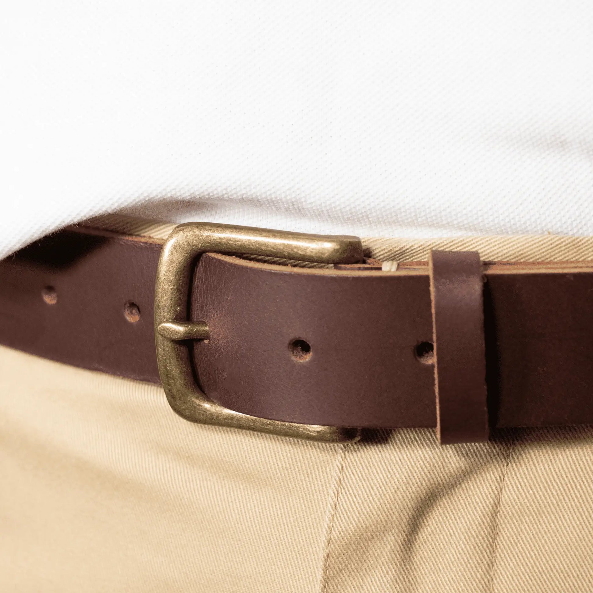Close-up of a men's brown genuine leather belt, styled with tan trousers and white t-shirt to showcase the stylish simplicity and rustic look of this NZ made accessory.