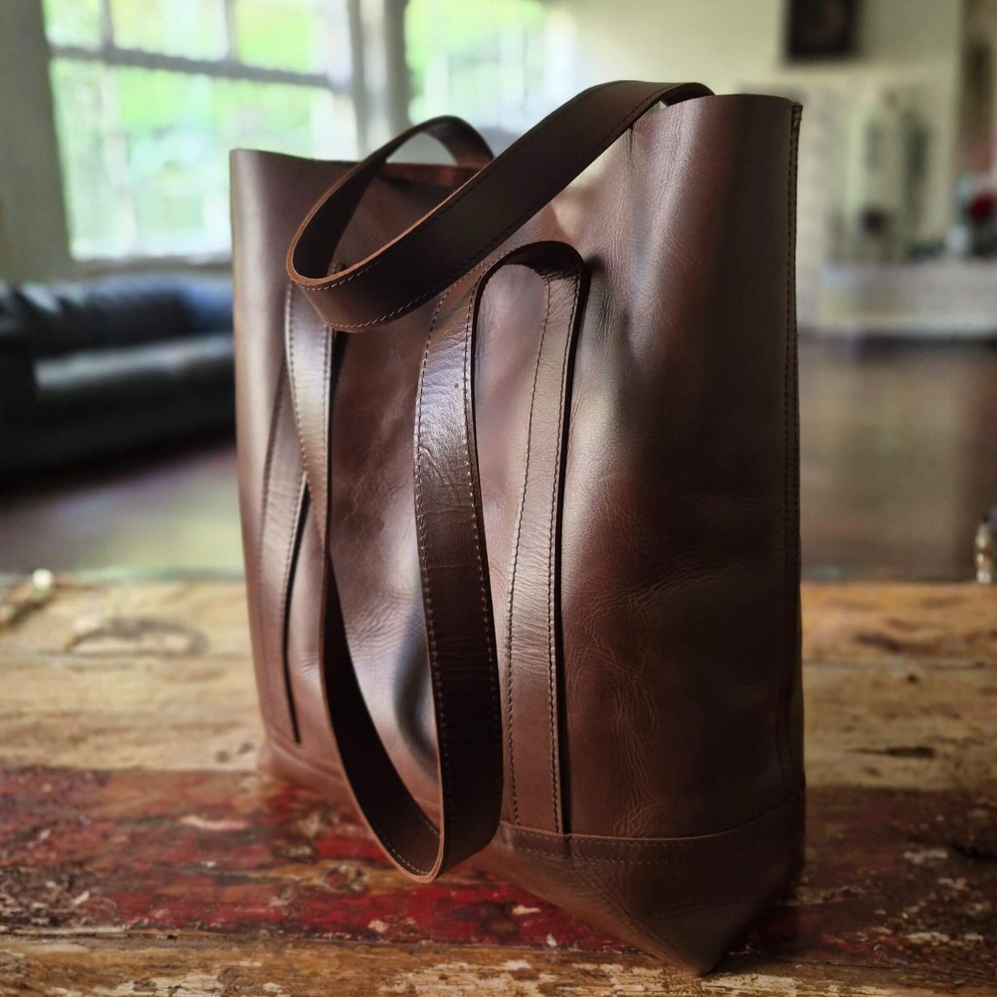 Chestnut brown leather tote bag on a wooden surface with a blurred indoor background