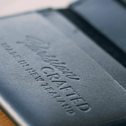 Close-up of embossed 'Parisian Crafted' logo on an open black leather folded card wallet, showcasing premium craftsmanship.