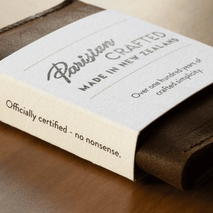 Close-up of a brown leather folded card wallet in white card packaging, displaying the "Parisian Crafted Made in New Zealand" logo.
