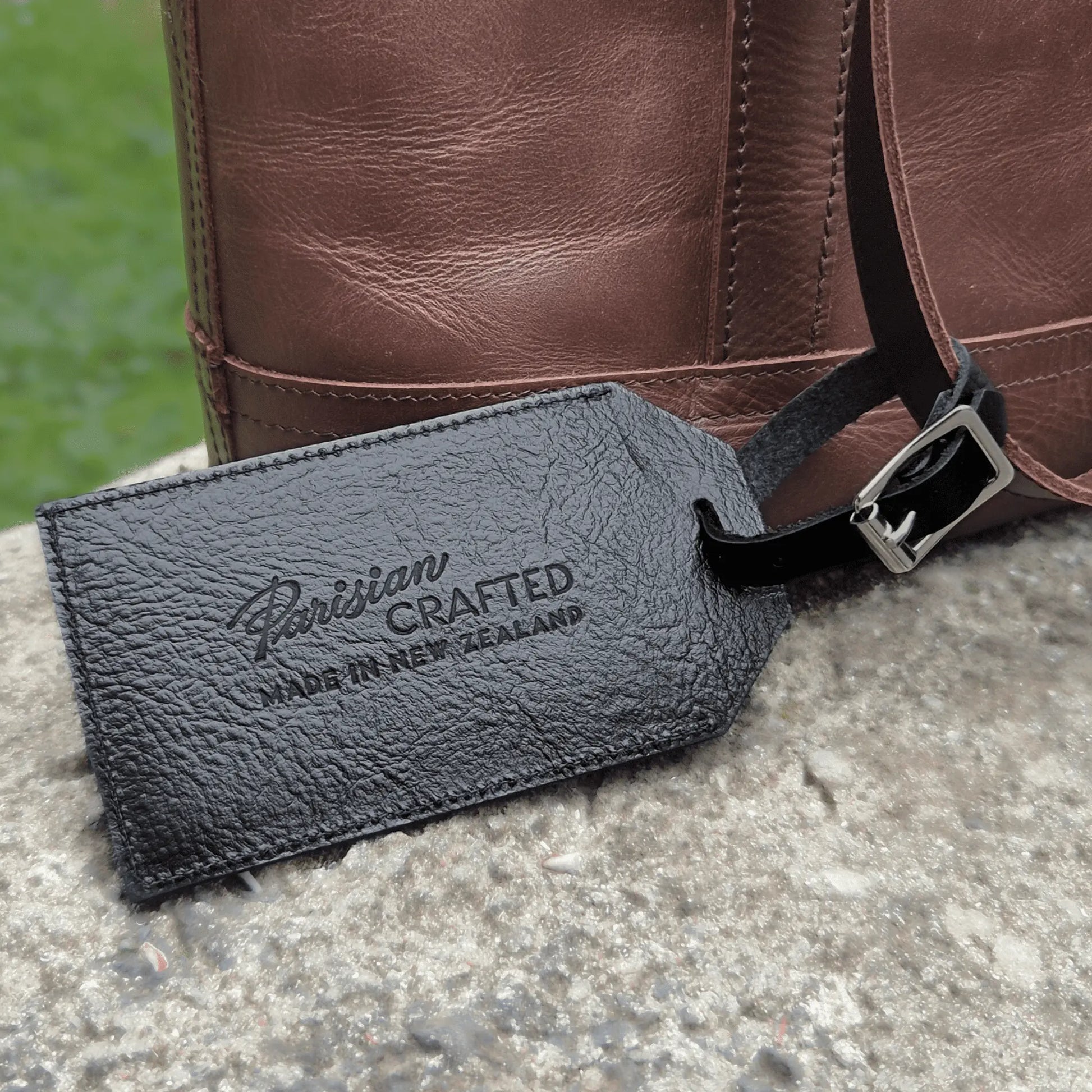Black leather luggage tag with 'Parisian Crafted' branding on a brown leather bag.