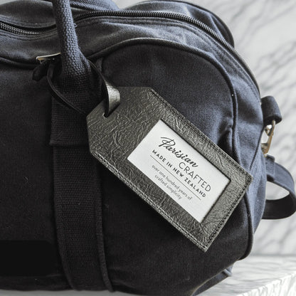 Navy duffel bag with a black leather tag displaying 'Parisian Crafted' on a light background
