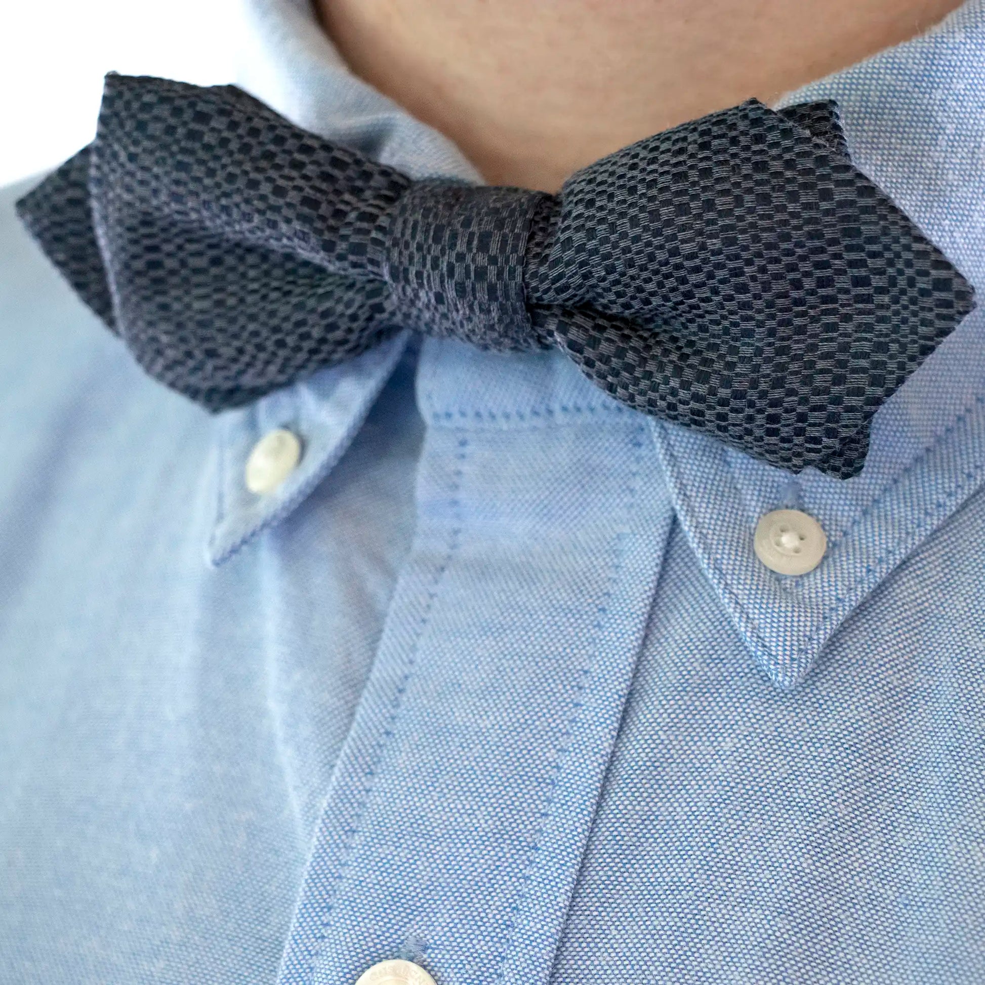 A close up of the Slate Blue Textured Bow Tie worn with a Blue Button Down Shirt.