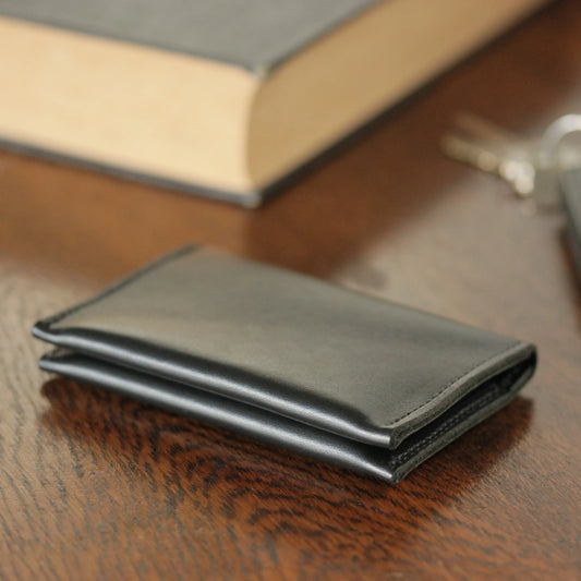 A Black Leather Folded Card Wallet sitting on a wooden table