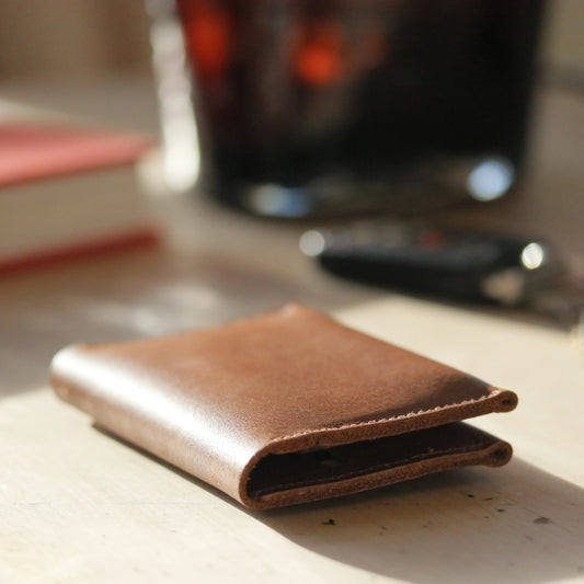 A close up of a Tan Leather Folded Card Wallet sitting in the sun on a wooden table