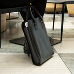 The Black Leather Business Tote resting against a chair leg.