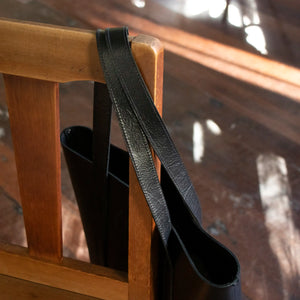 A close up of the Black Everyday Leather Tote hanging off the back of a wooden chair.